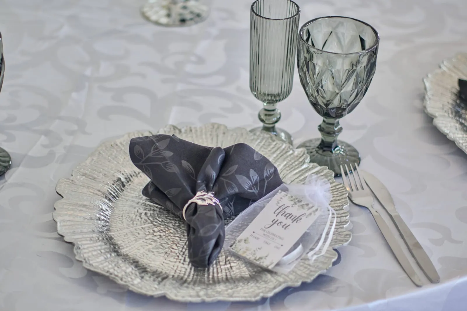 A place setting: textured charger, dark napkin and a thank-you tag