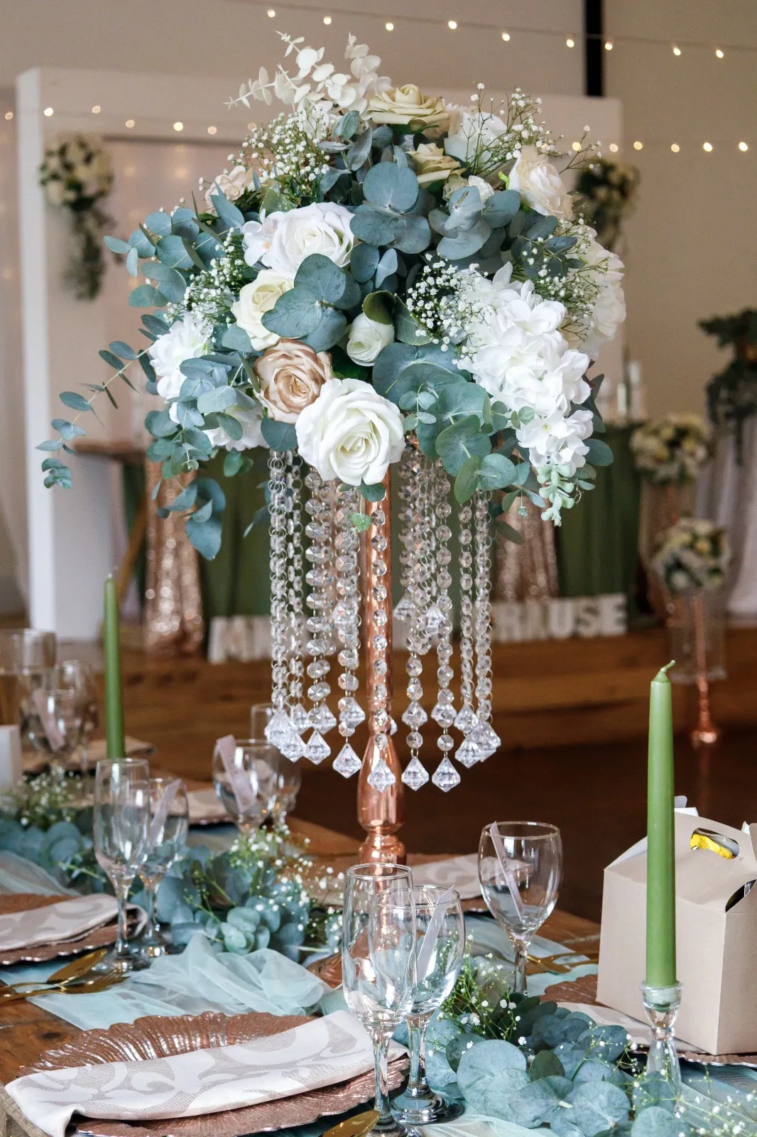 A tall floral centrepiece in white and sage on a crystal stand