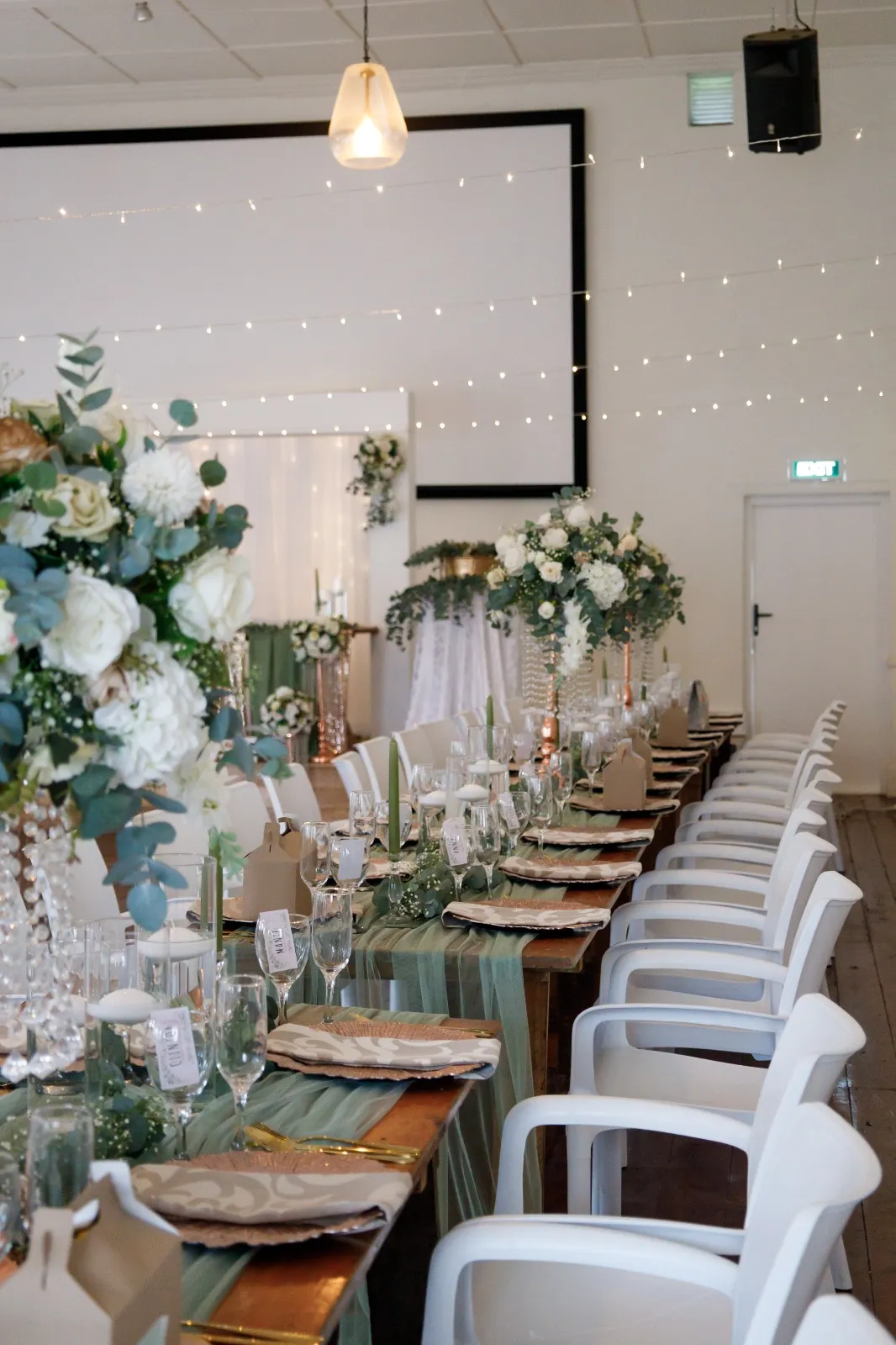 A long table dressed with white florals and fairy lights above