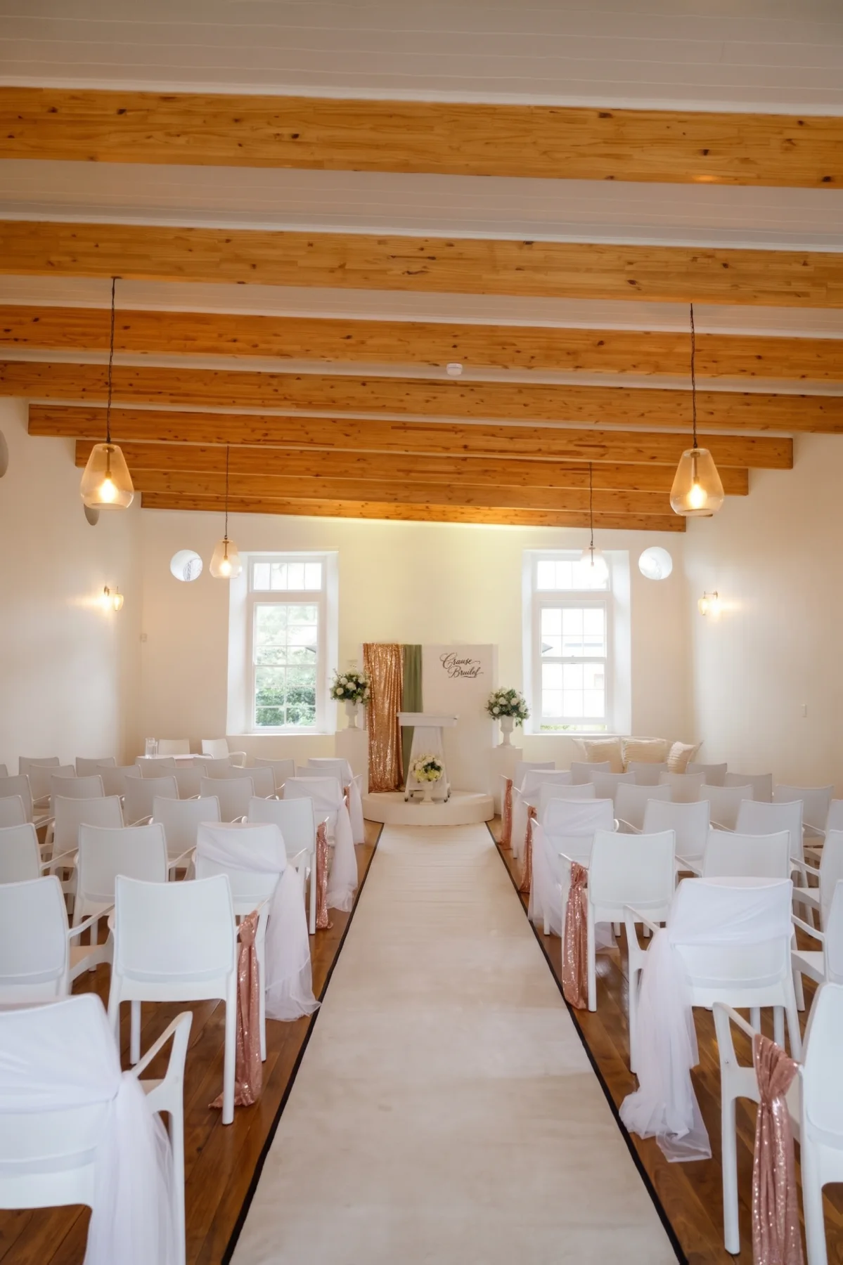 Hall 2 set for a ceremony: two blocks of white chairs either side of a centre aisle, exposed timber roof beams above