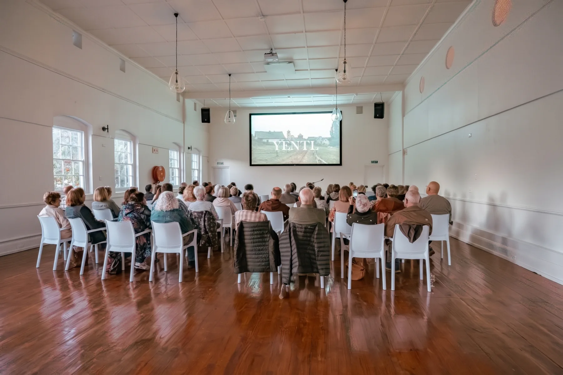 An audience on white chairs watching Yentl on the big screen, the first film shown in the restored hall